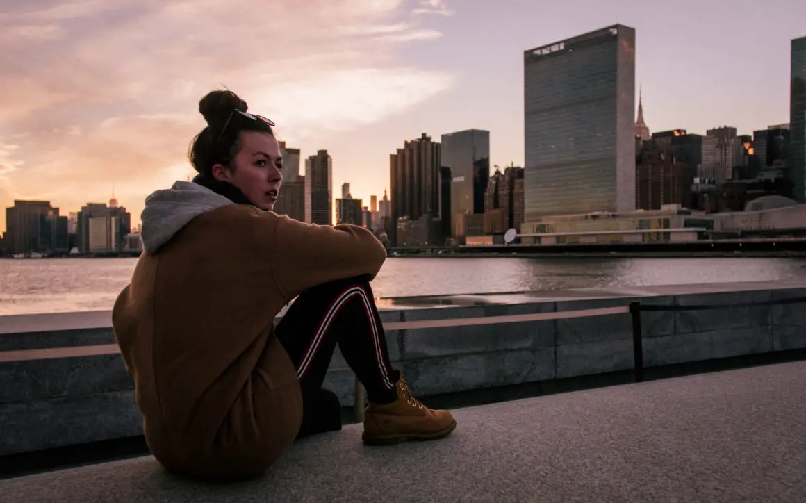 Katie looking out to a sunset behind a New York skyline. Photo was taken on Roosevelt Island.