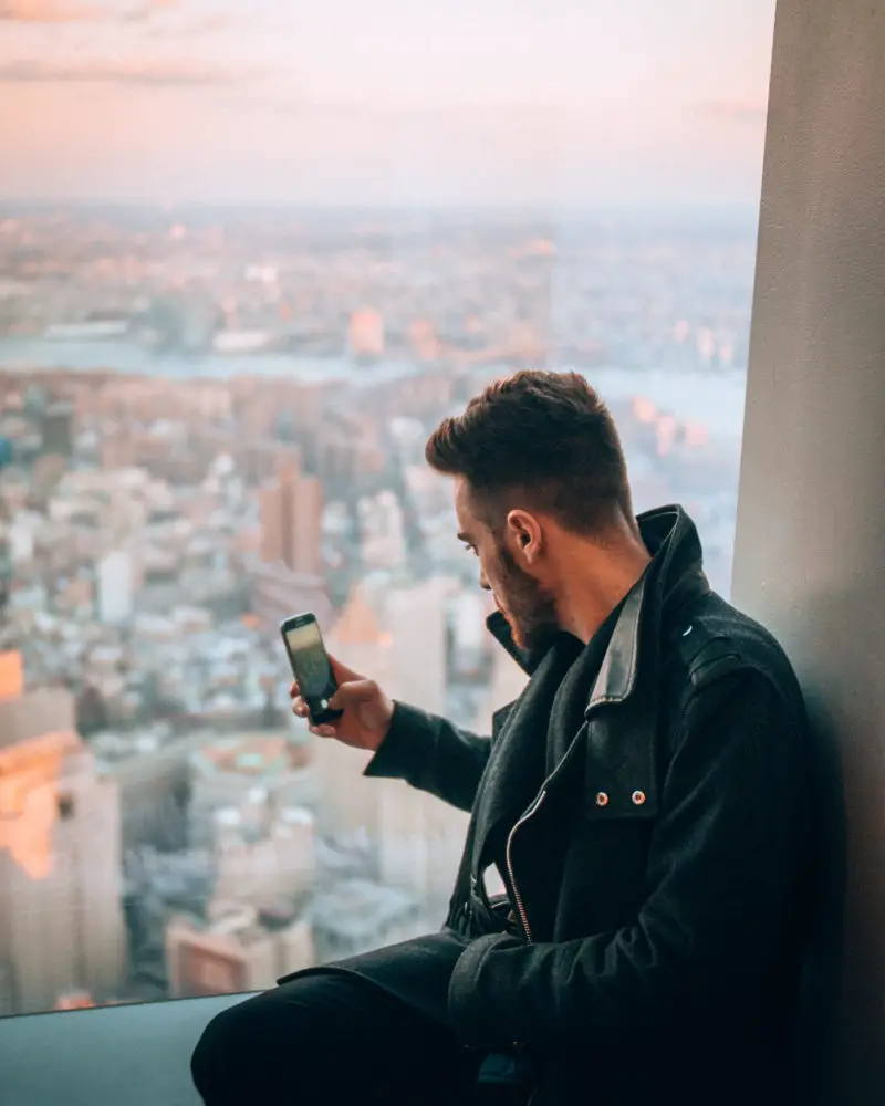 Man taking a photograph of the city from behind the glass up the top of the Freedom Tower.