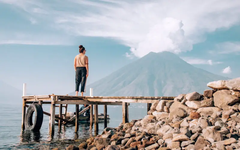 Katie standing in a remote location on a pier looking out to a distant volcano.